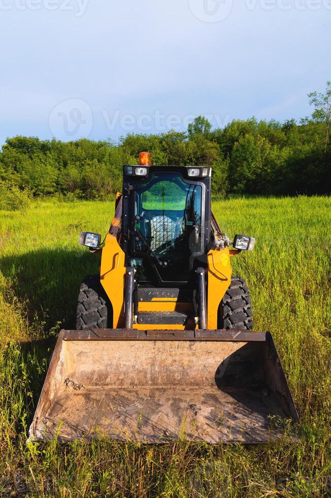 Small bulldozer will level the ground, preparing for new housing construction. Construction equipment on green grass in a field photo
