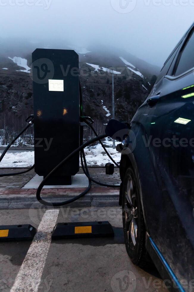 Low key. A car is parked near an electric filling station and is filling up. Electric filling stations in highland areas photo