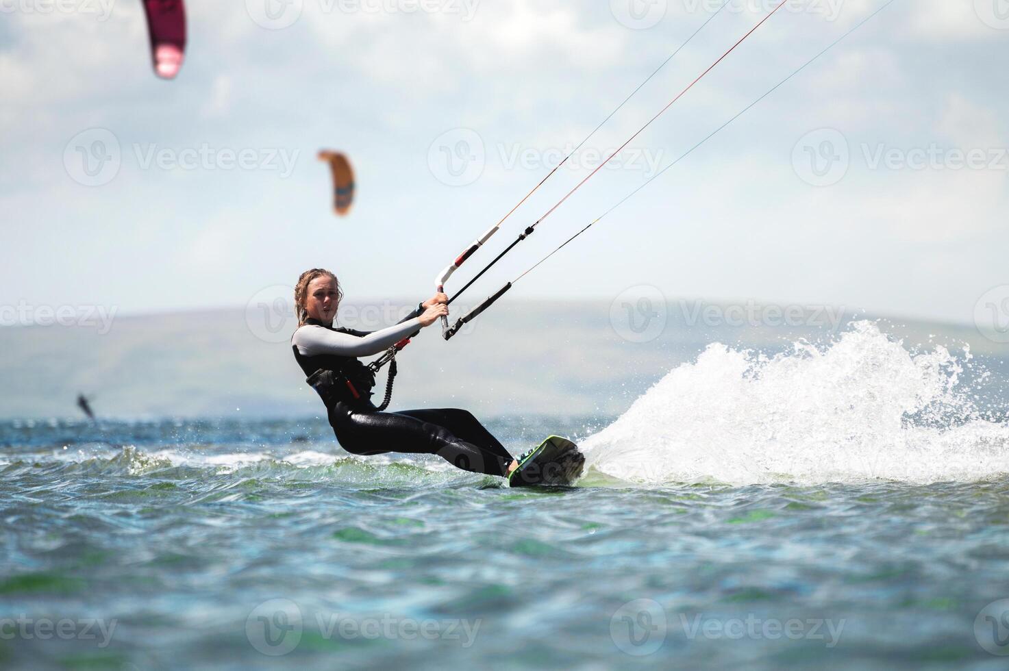 CLOSE UP, Fit Caucasian tourist kiteboarding along peninsula. Relaxed young woman surfing boarding and exploring Mediterranean coastline on sunny summer day photo