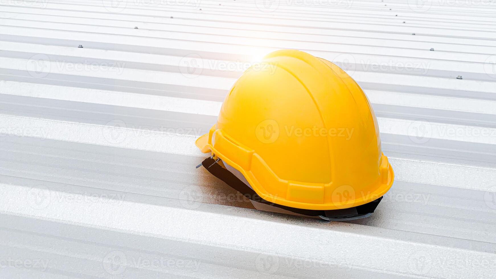 Features a bright yellow safety helmet resting on a clean metal roof, bathed in sunlight, highlighting safety in construction environments. Perfect for representing industry, safety protocols. photo