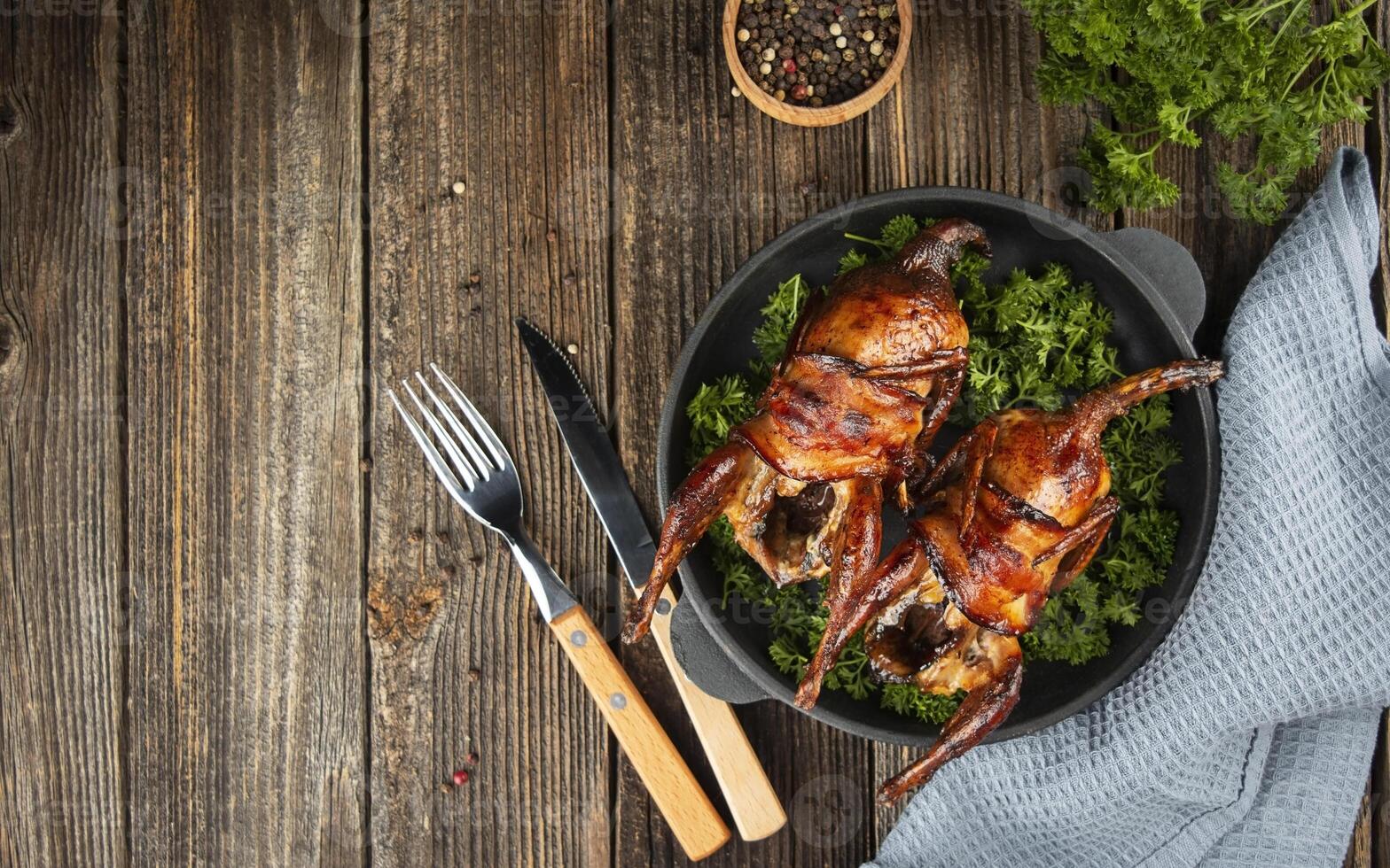 Baked quail with herbs on a wooden table. Side view. Banner. Copy space. photo