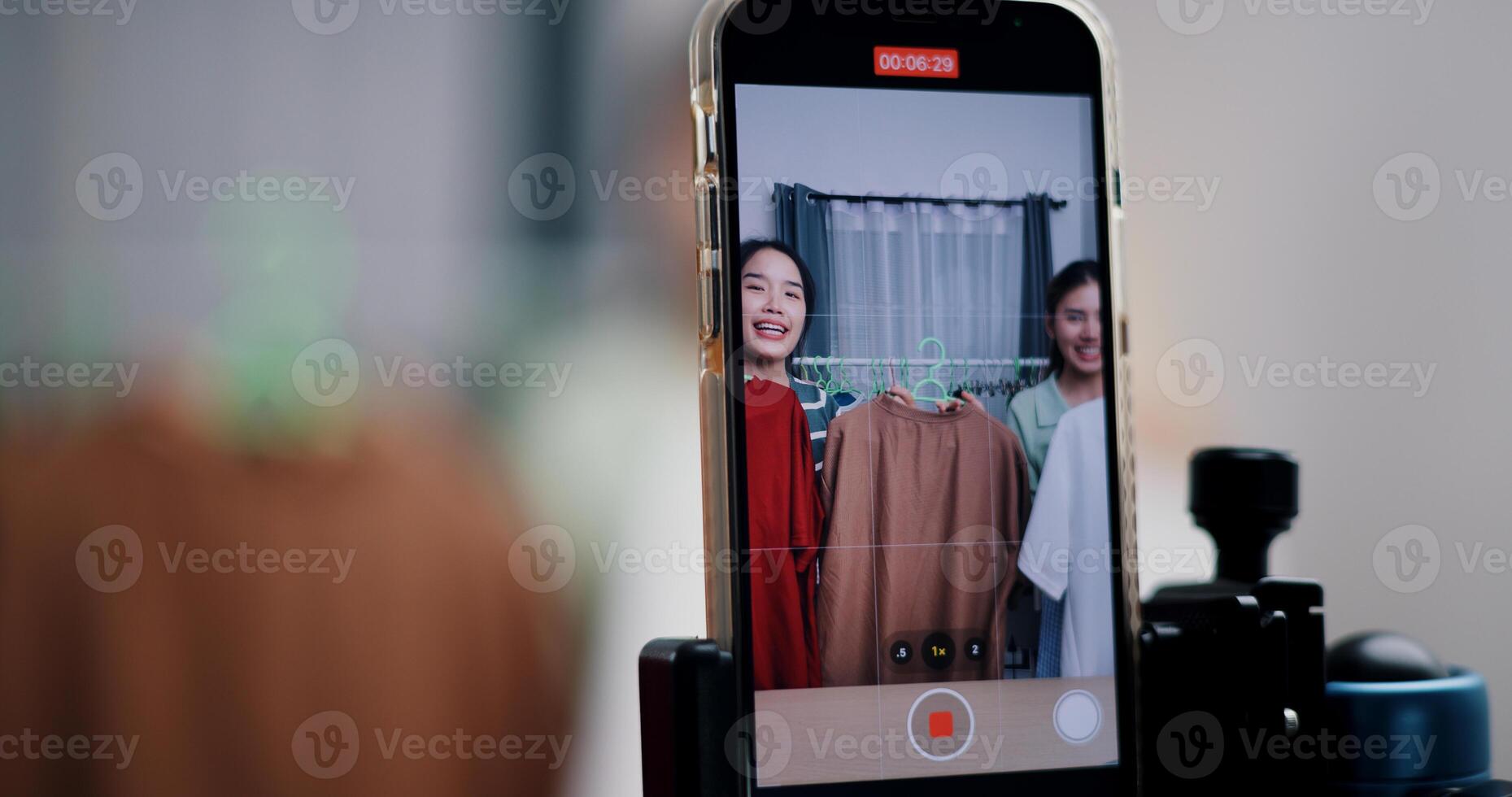 Selective focus on mobile phone of Two cheerful woman influencers are live streaming sell clothes on social media or blogging in home studio. Remote buying, Online shopping. photo