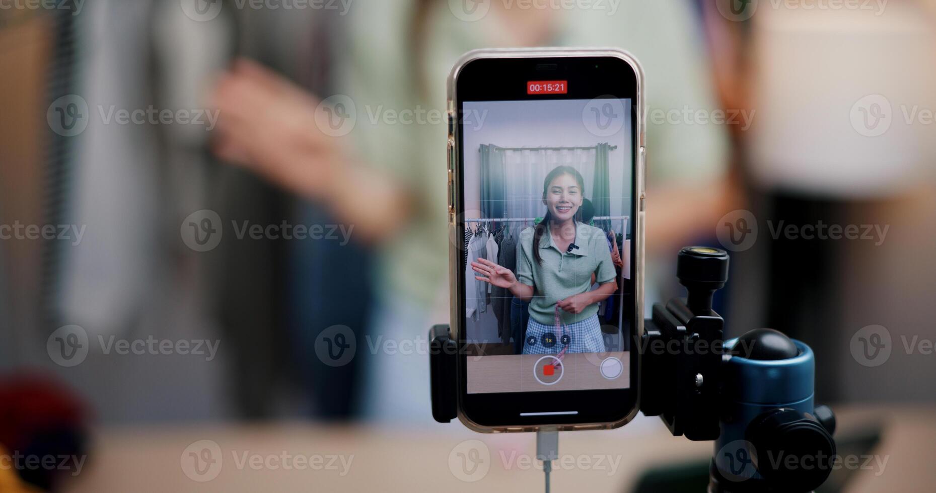 Selective focus on mobile phone of Two cheerful woman influencers are live streaming sell clothes on social media or blogging in home studio. Remote buying, Online shopping. photo