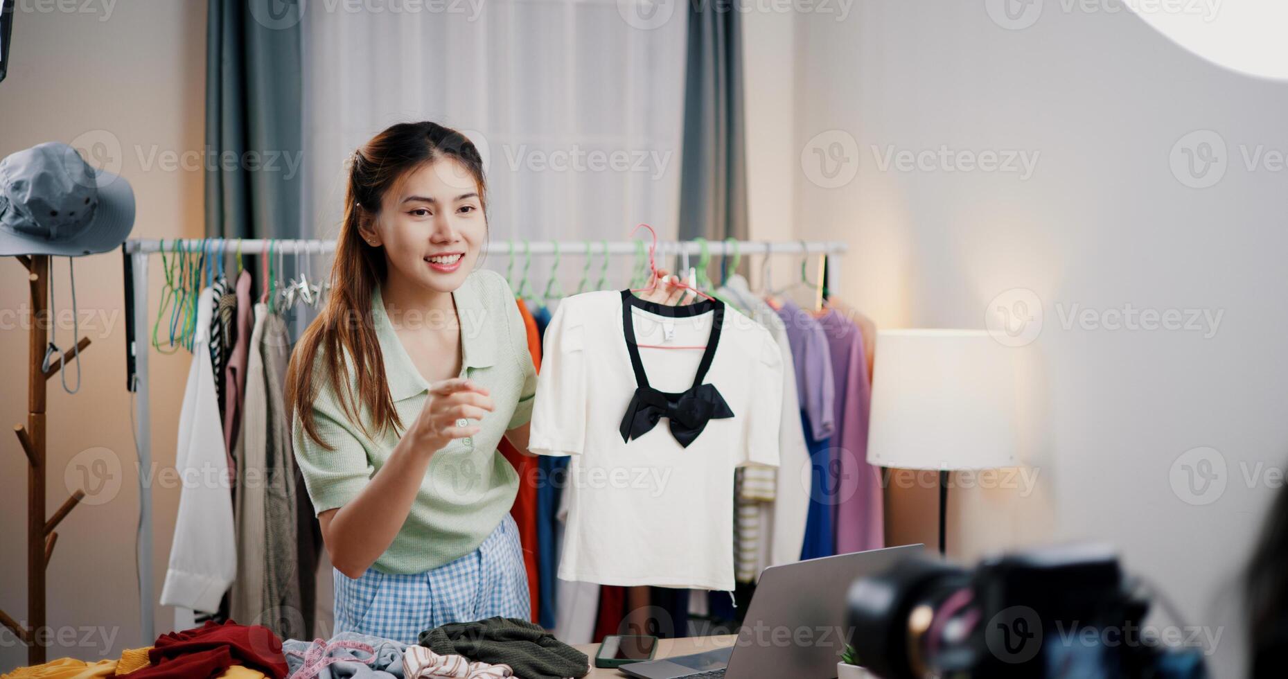 Portrait of Cheerful woman influencer is live streaming sell clothes on social media or blogging in home studio. Remote buying, Online shopping. photo