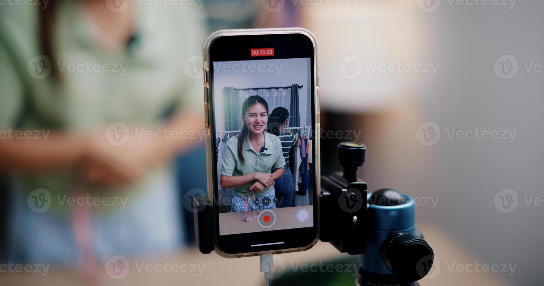 Selective focus on mobile phone of Two cheerful woman influencers are live streaming sell clothes on social media or blogging in home studio. Remote buying, Online shopping. photo