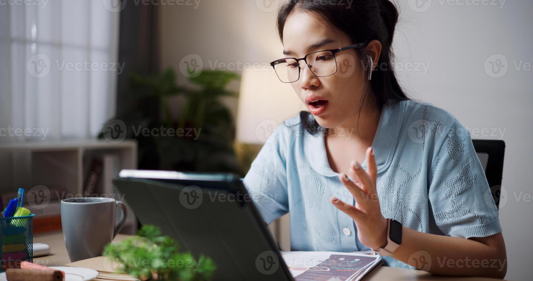 Portrait of Female freelancer sitting at desk wear wireless headphones having call to explain work to coworkers via digital tablet in home office. photo