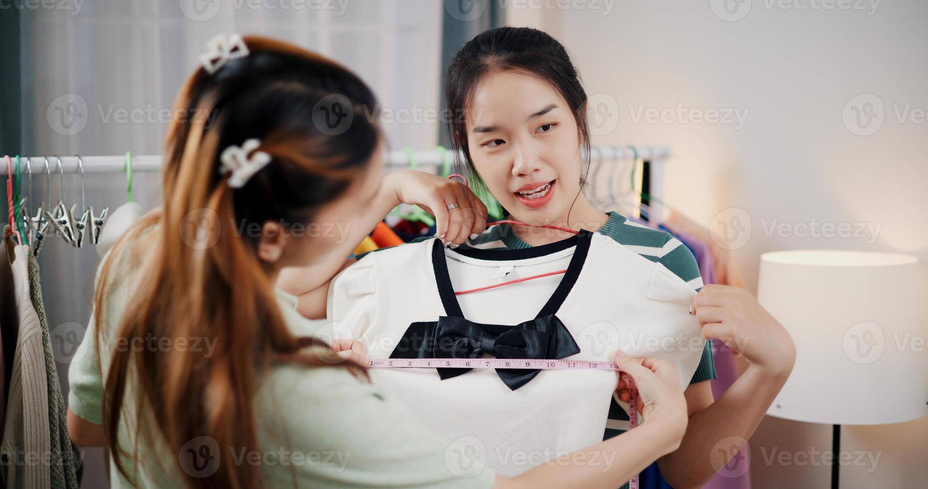 Portrait of Two cheerful woman influencers are live streaming sell clothes on social media or blogging in home studio. Remote buying, Online shopping. photo