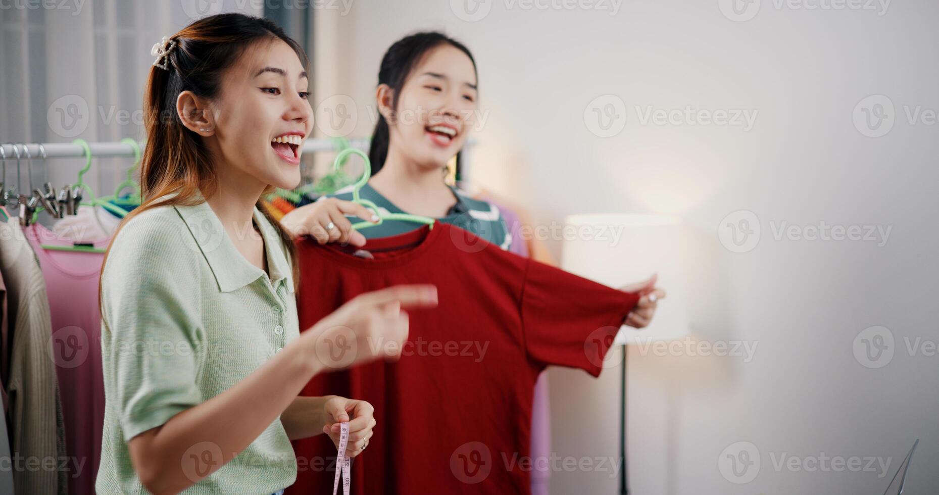 Portrait of Two cheerful woman influencers are live streaming to promote a clothing sell during a flash sale on social media or blog in a home studio. Remote shopping, online shopping. photo