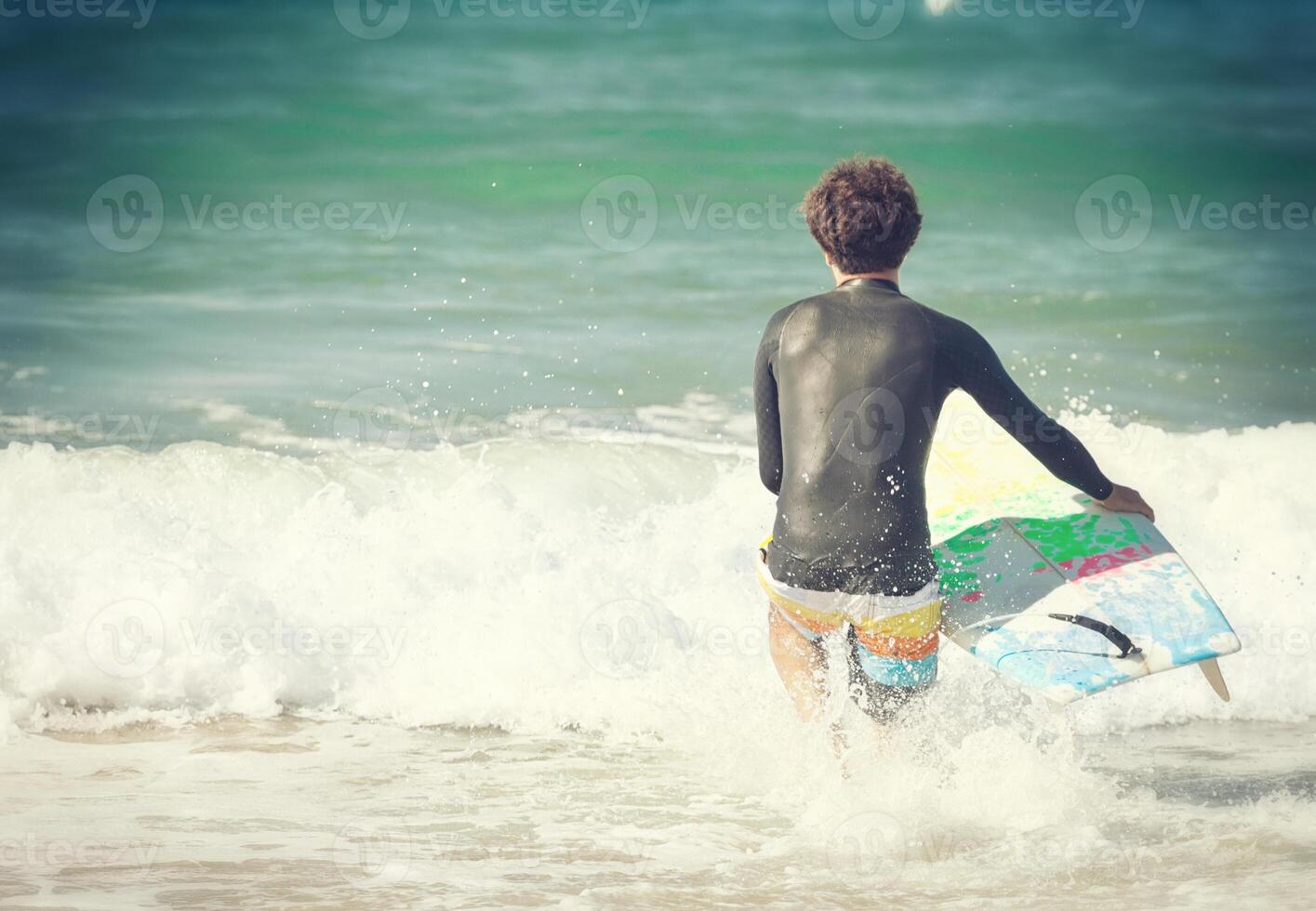 A man in a wet suit holding a surfboard in the ocean photo