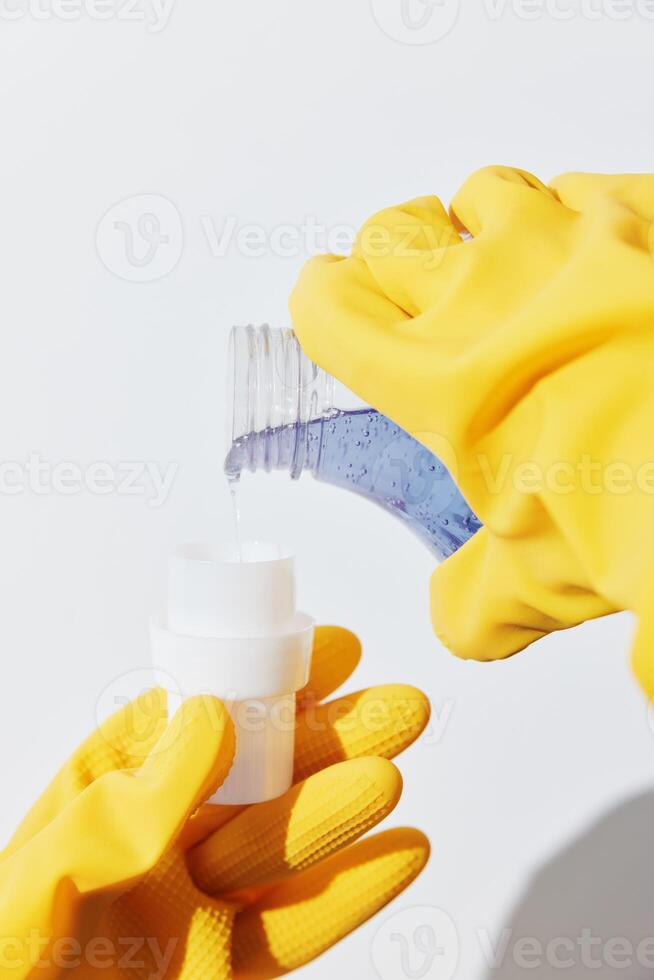 Woman pouring hand sanitizer from one bottle to another wearing yellow gloves. photo