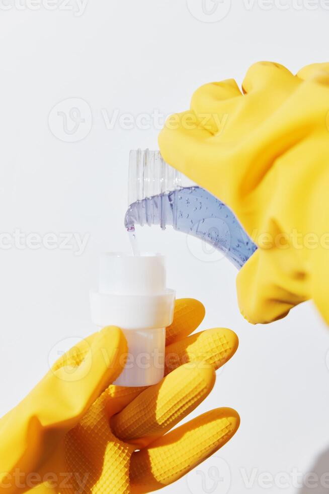 Woman wearing yellow rubber gloves holding a bottle of hand sanitizer on a white surface. photo