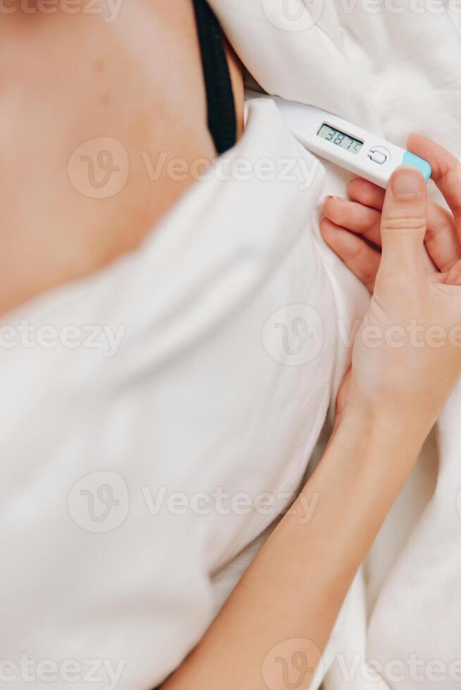 Woman in bed holding digital thermometer. white sheets and pillow. temperature measurement concept. photo