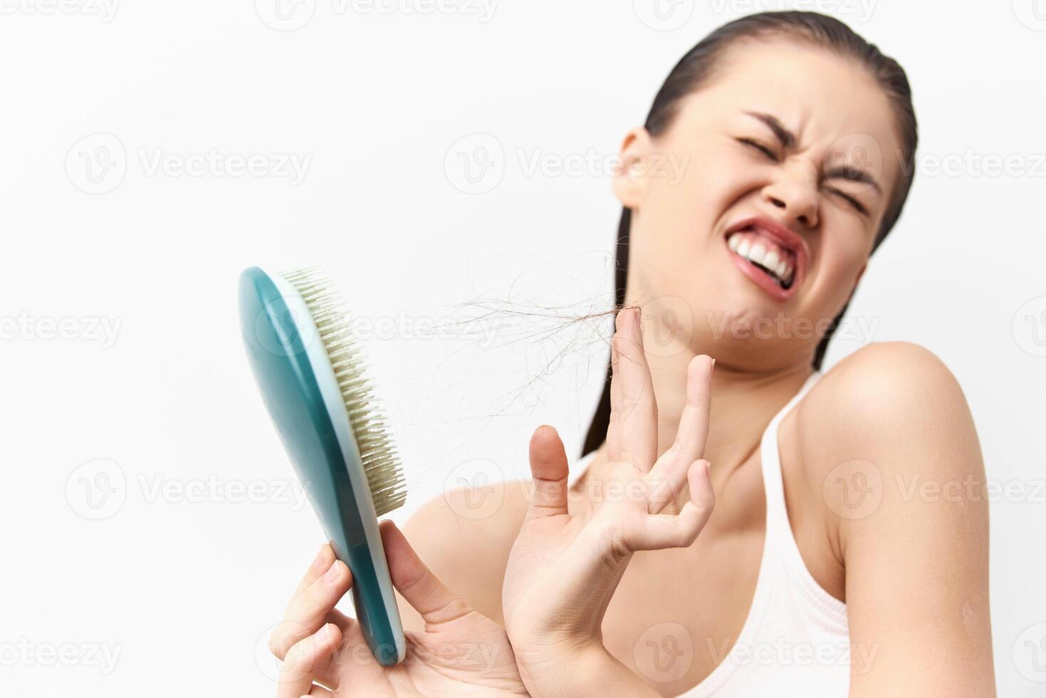 A young woman displaying frustration while trying to brush her hair, showcasing tangled hair strands photo