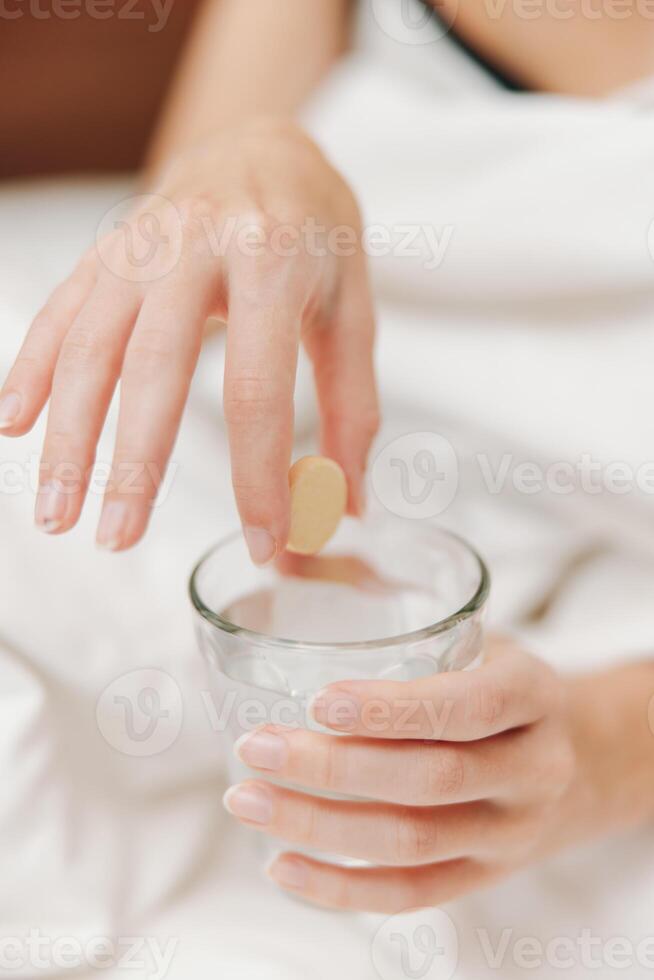 Person lying in bed holding a pill and a glass of water. a concept of taking medication in the photo