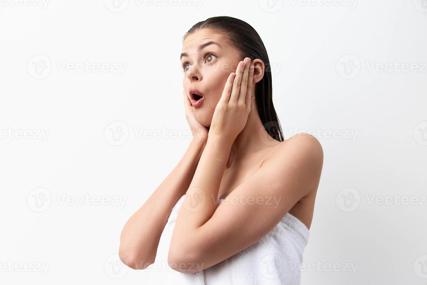 surprised young woman with wet hair holding her face in astonishment, wearing a towel, set against a photo