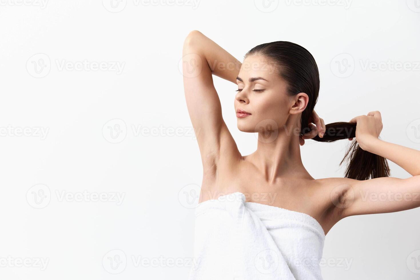 A beautiful woman with a calm expression pulls her hair back while wrapped in a towel, emphasizing photo
