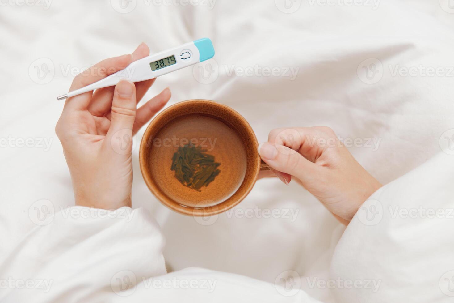 Ill patient lying in bed with a cup of tea and a thermometer on white sheets. a person feeling photo