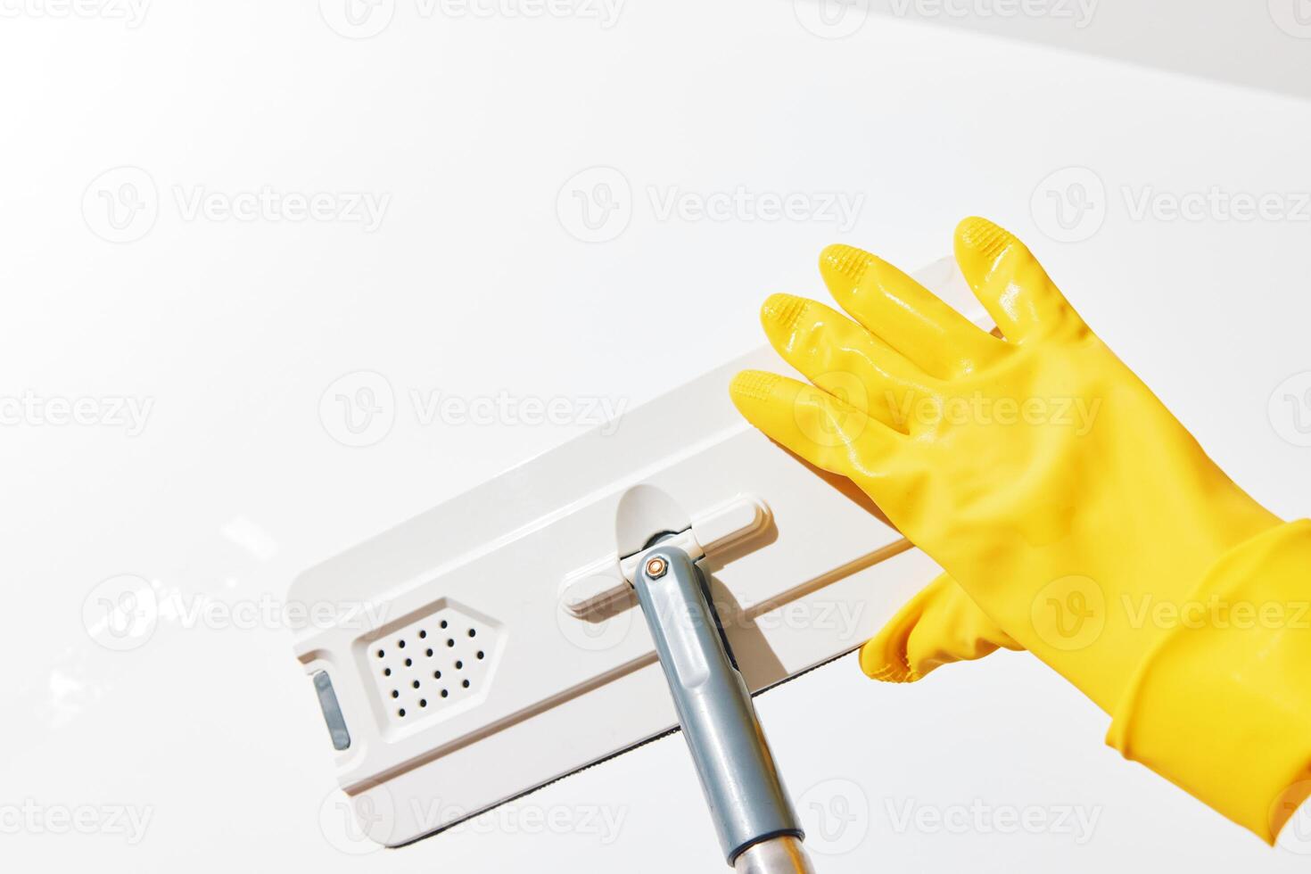 Cleaning woman in yellow rubber gloves using a mop with a yellow rubber glove on the end to clean a photo