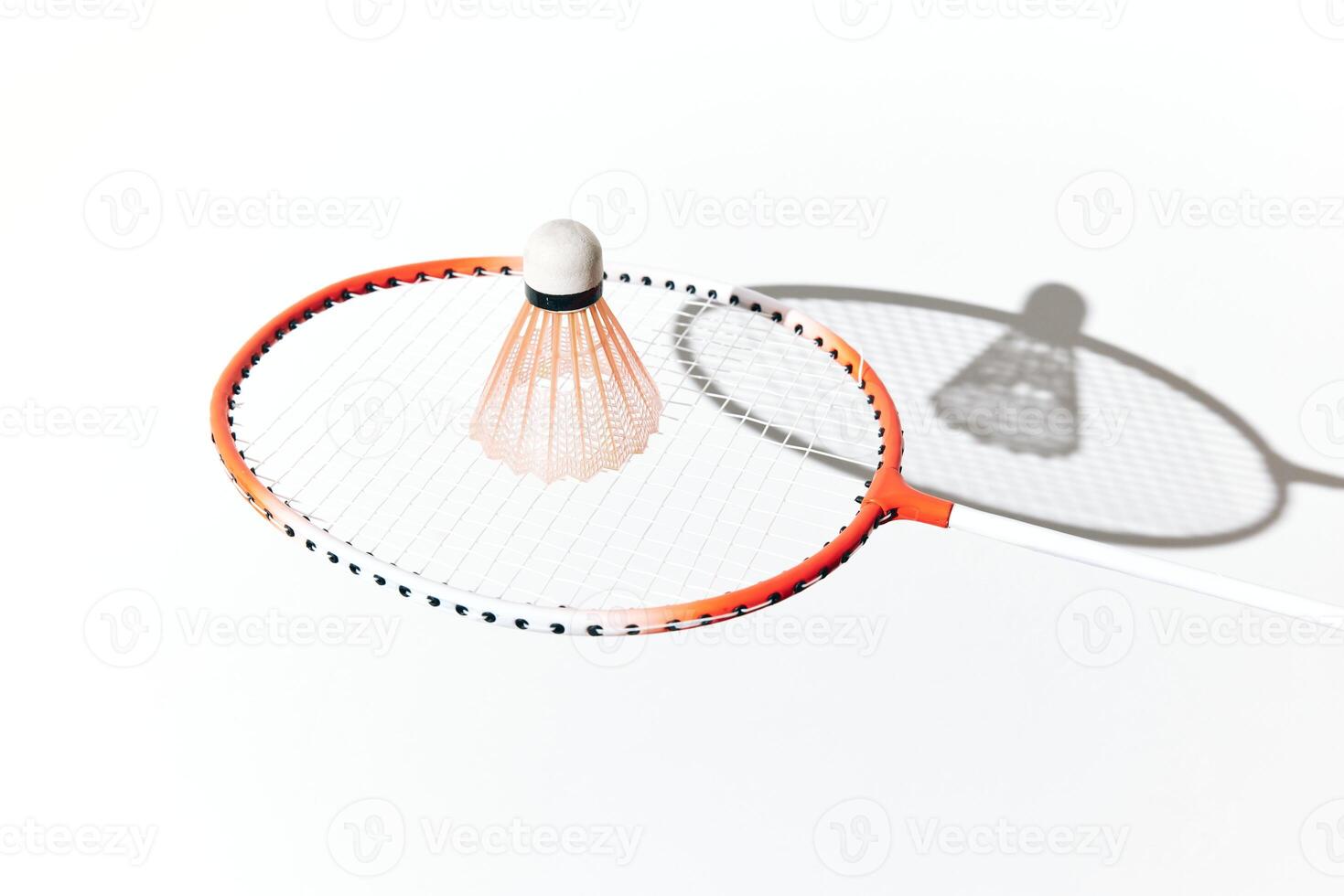 Orange and white badminton racket and shuttlecock casting a shadow on a white surface. photo