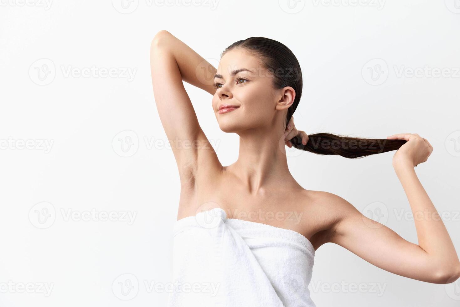 a young woman with long hair holds her hair back while smiling, showcasing healthy skin and a photo