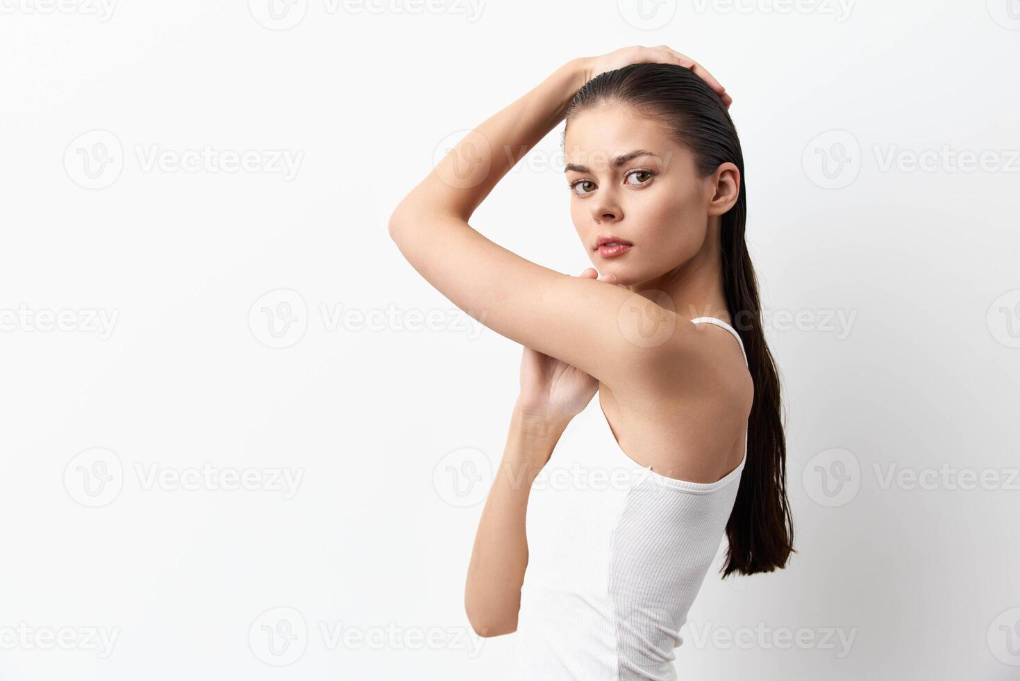 A young woman stands elegantly in a white tank top, posing against a minimalistic white background photo