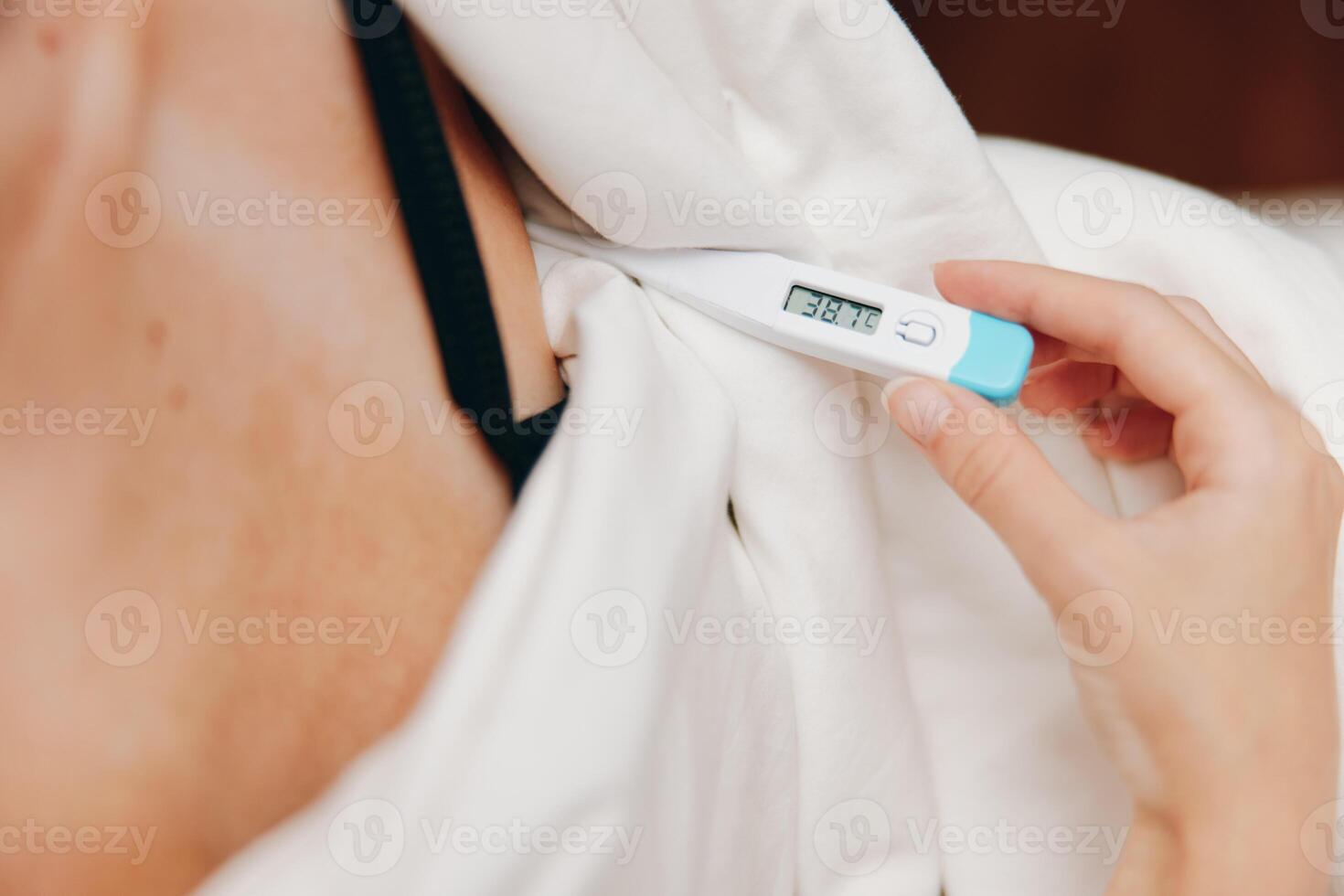Woman holding an electronic thermometer in hand, wearing a white tank top and bra. photo
