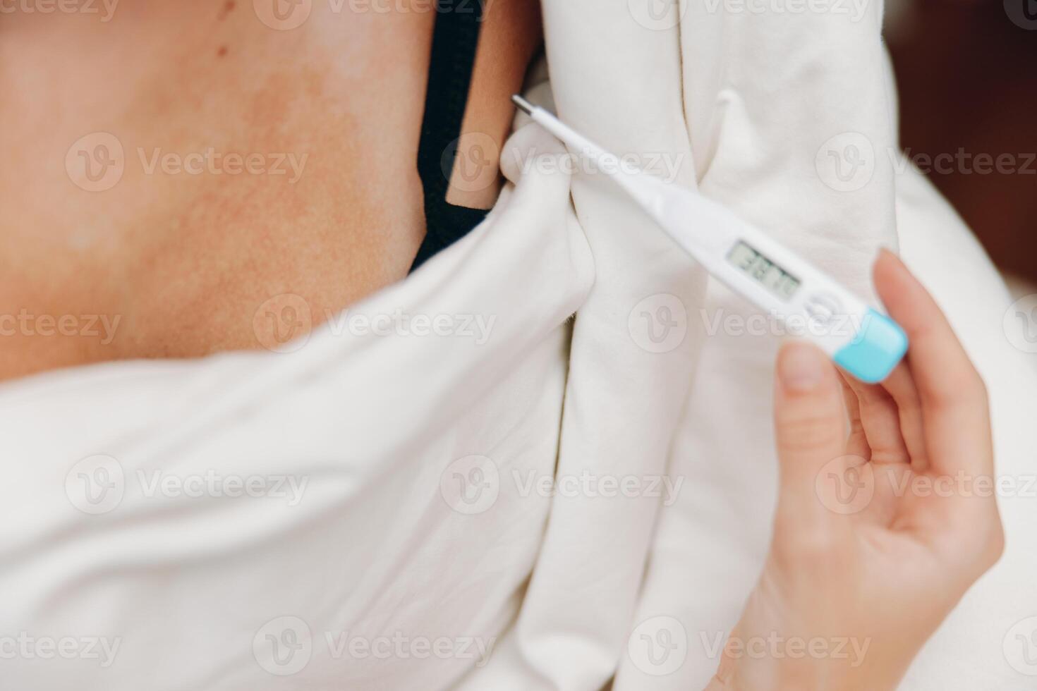 Woman in white shirt and bra holding electronic thermometer in hand. photo