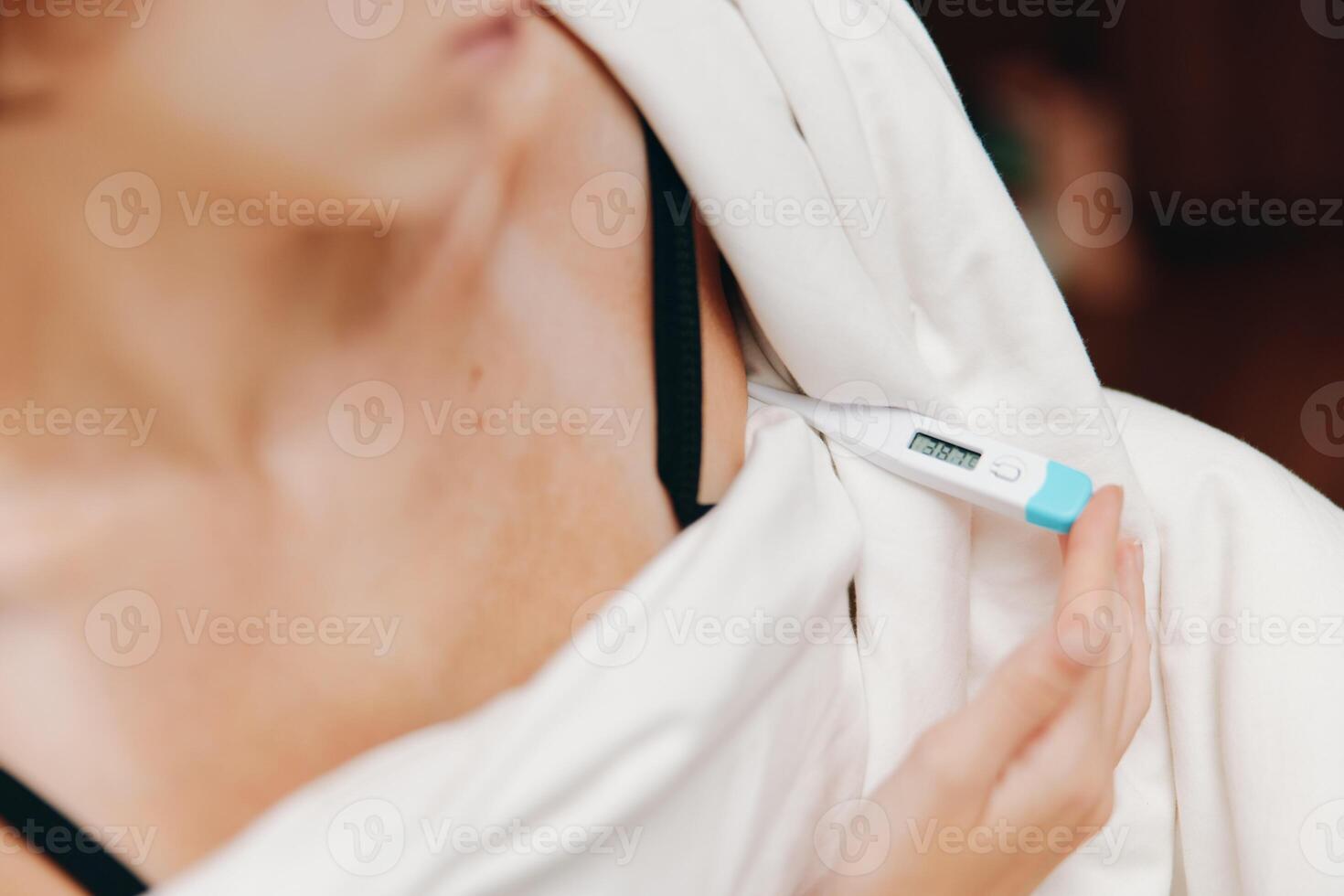 Woman in white shirt holding electronic thermometer, black bra visible. photo