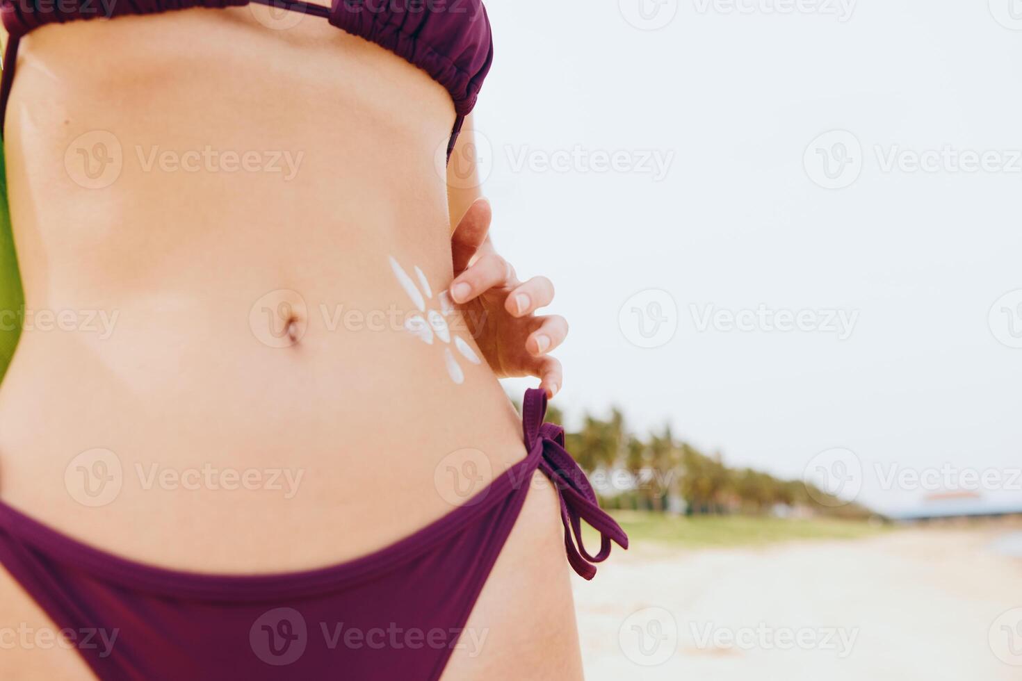 Woman in purple bikini standing on the beach with hands on hips and a white sticker on her stomach. photo