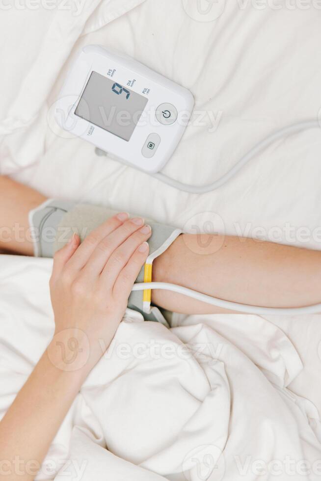 Woman lying in bed with a blood pressure monitor and cuff on her arm. monitoring her blood pressure photo