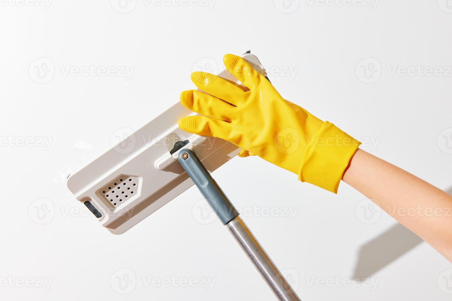 Woman holding yellow rubber glove mop against white wall. photo