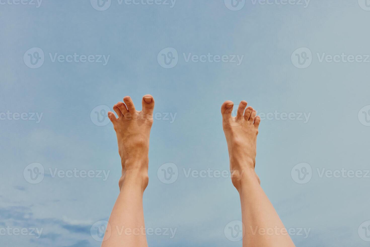Legs of person raised high in the air against a clear blue sky with a few fluffy clouds in the photo