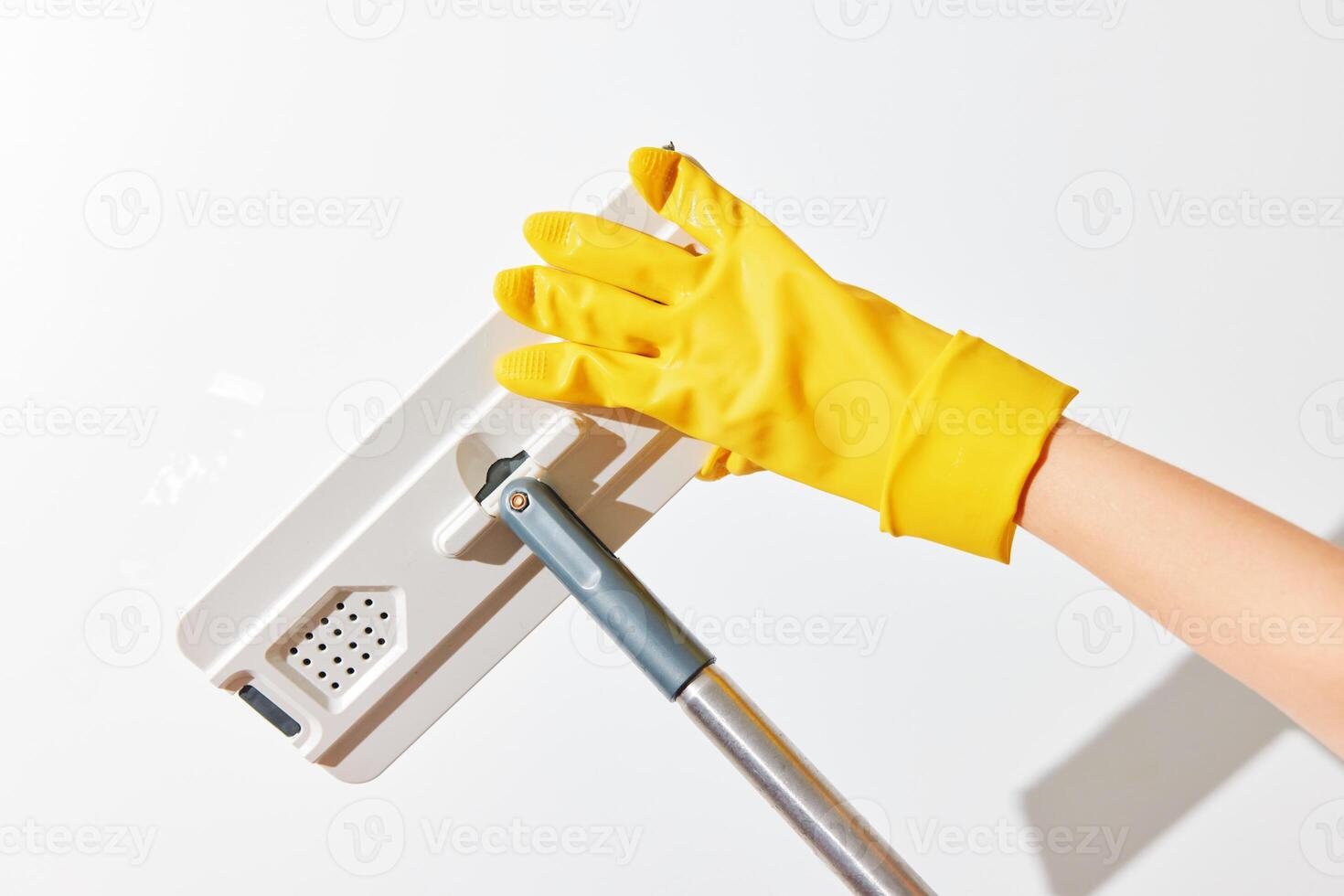 Woman in yellow gloves holding yellow mop against white wall. photo
