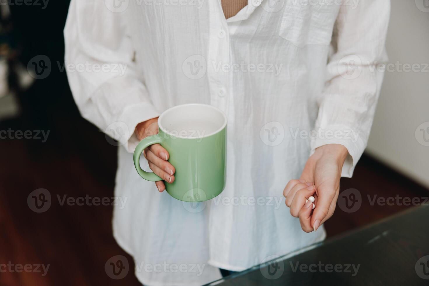 Woman in white shirt holding green coffee mug in front of table with glass of water. a simple and photo