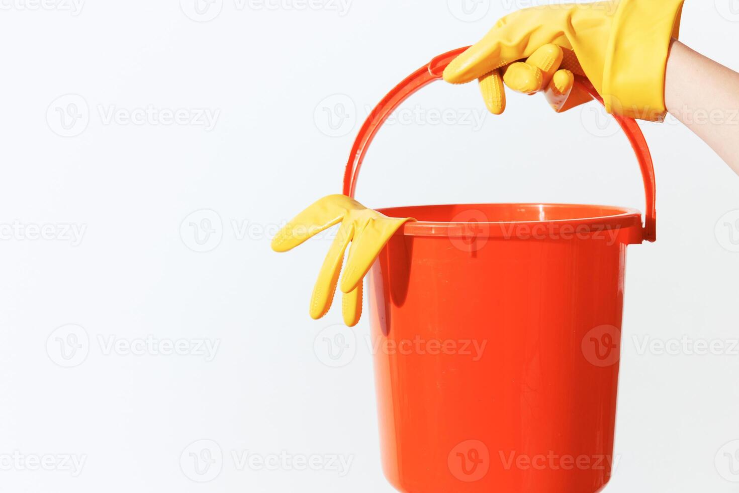 Person in yellow rubber gloves holding an orange bucket on white background. copy space available. photo