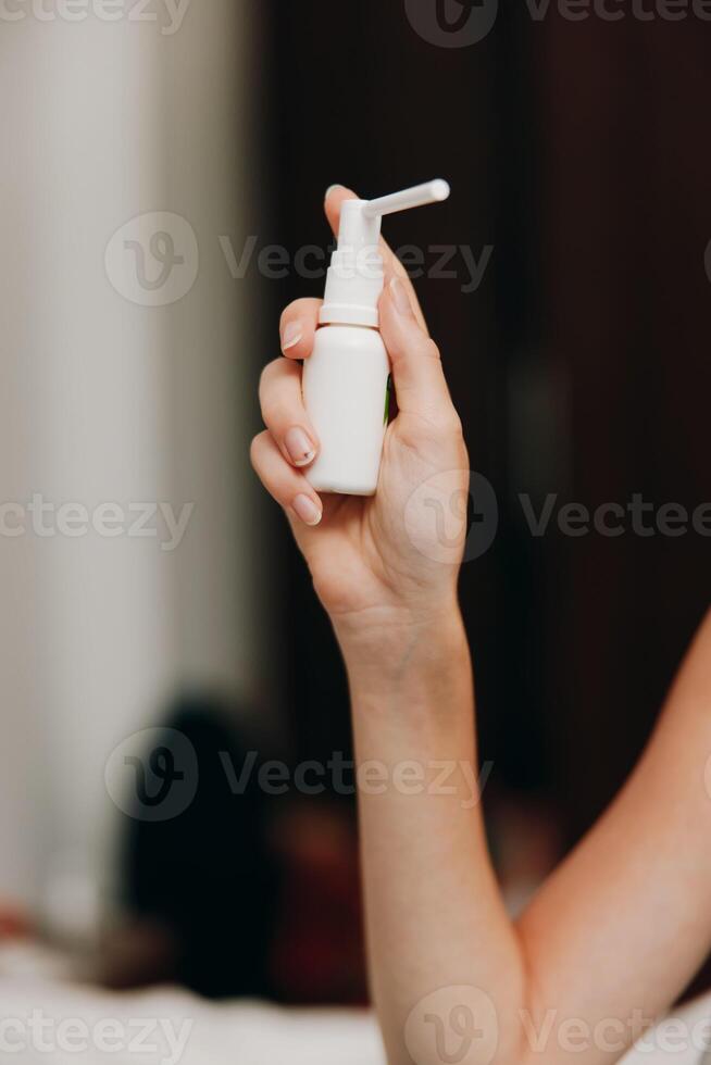 Woman holding hand sanitizer bottle while sitting on white bed. cleanliness and hygiene concept photo