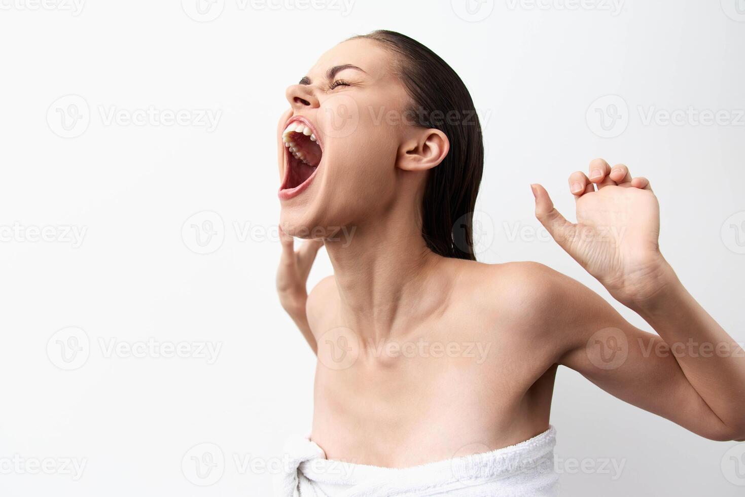 A woman with long hair is yawning with a relaxed expression, wrapped in a towel The background is photo