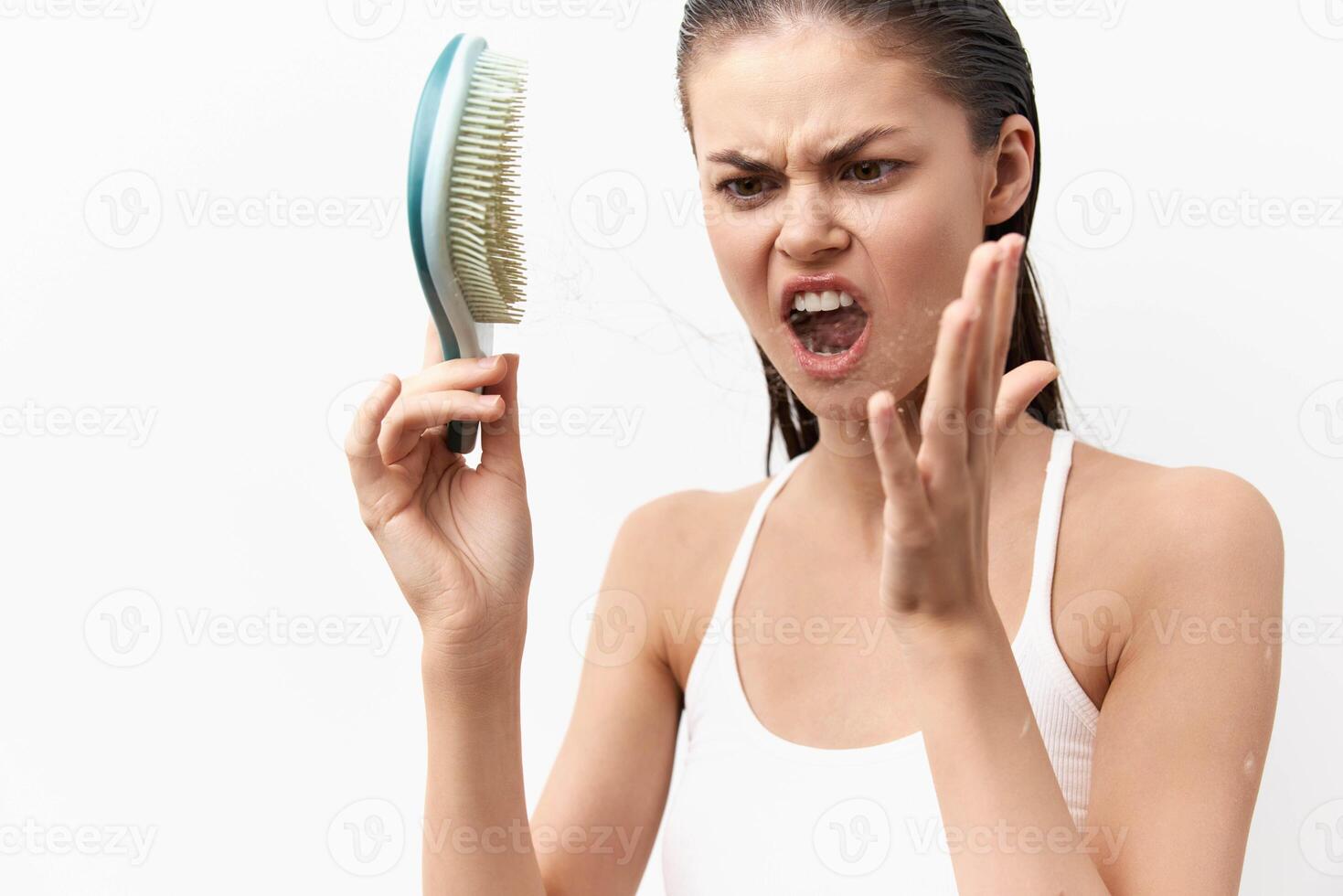 A young woman with wet hair is holding a hairbrush with a frustrated look, showing her annoyance at photo