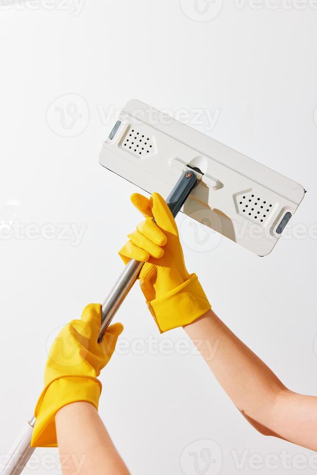 Woman cleaning white wall with mop and dusting brush in yellow gloves. photo