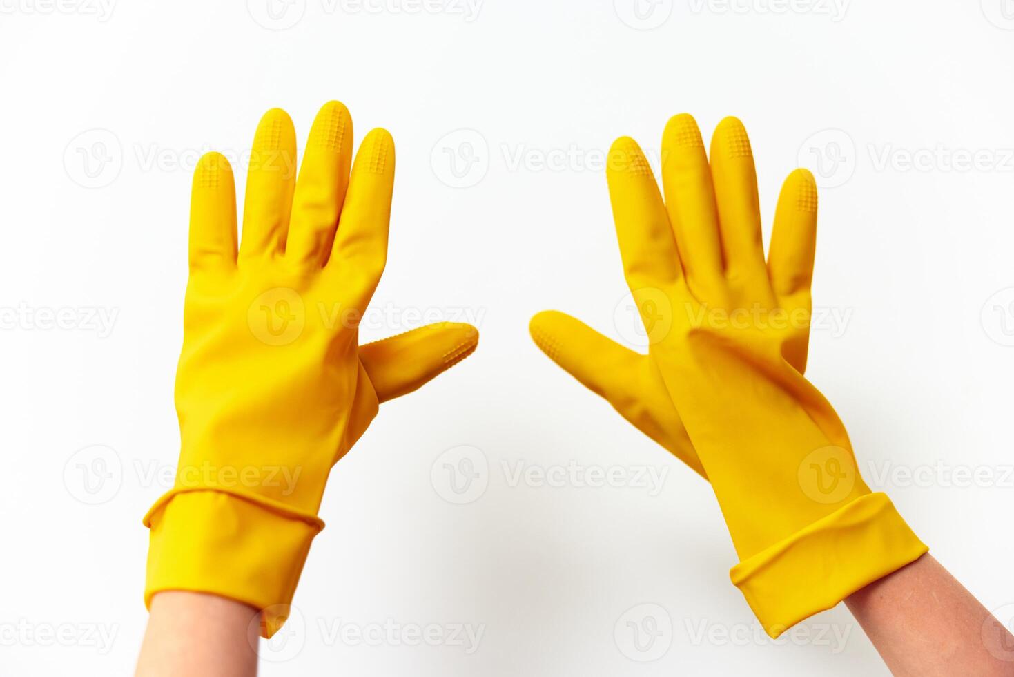 Rubber yellow gloves held up by a hand on a white surface. photo