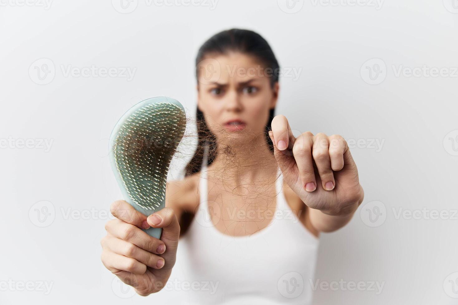 A young woman holding a hairbrush with hair strands caught in it, displaying a worried expression photo