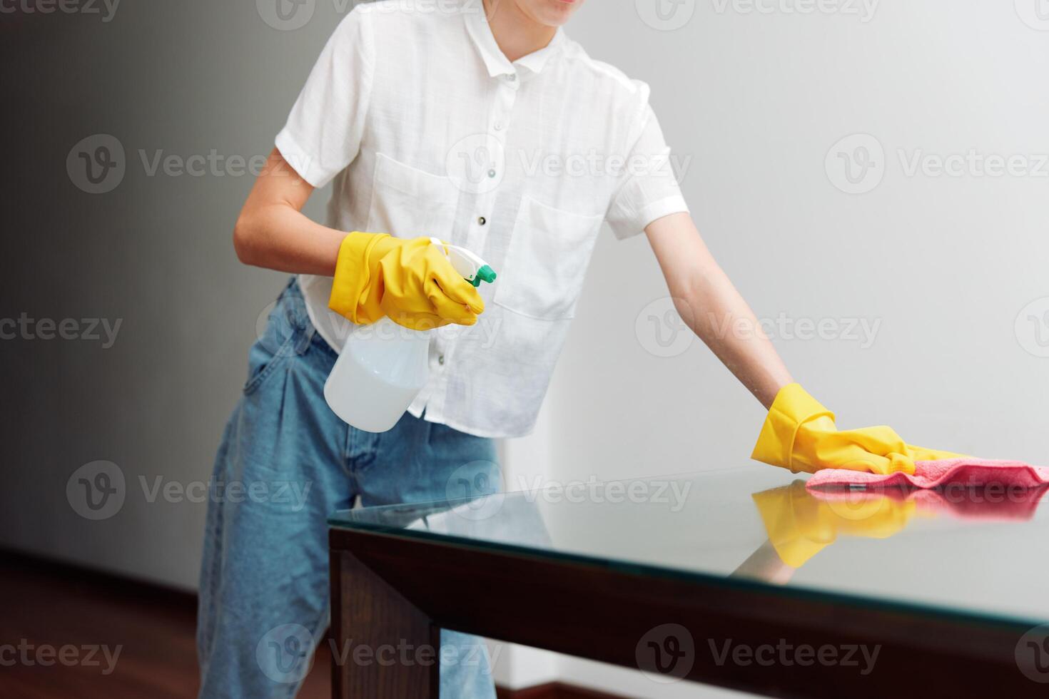 Woman in white shirt and yellow rubber gloves cleaning glass table with cleaning solution and rag. a photo
