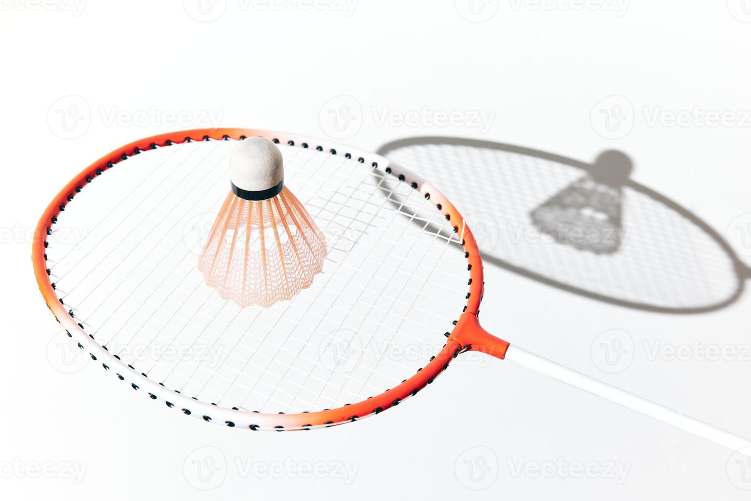 Badminton racket and shuttlecock on white surface with shadow. orange and white colors. photo