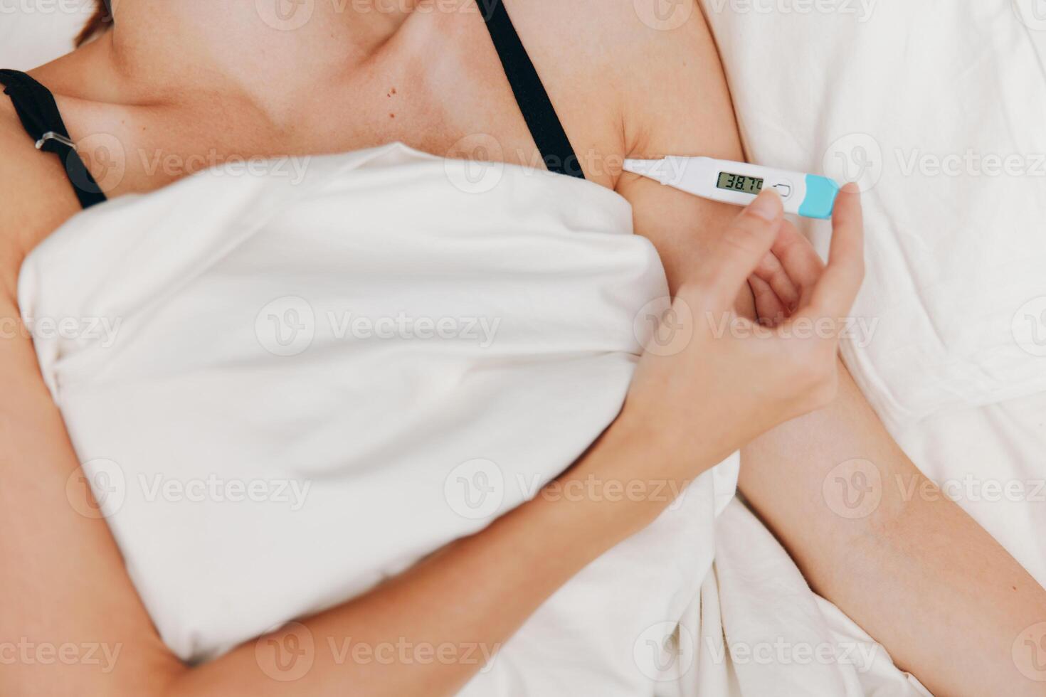 Woman lying in bed holding a thermometer with another thermometer on the bedside table. monitoring photo