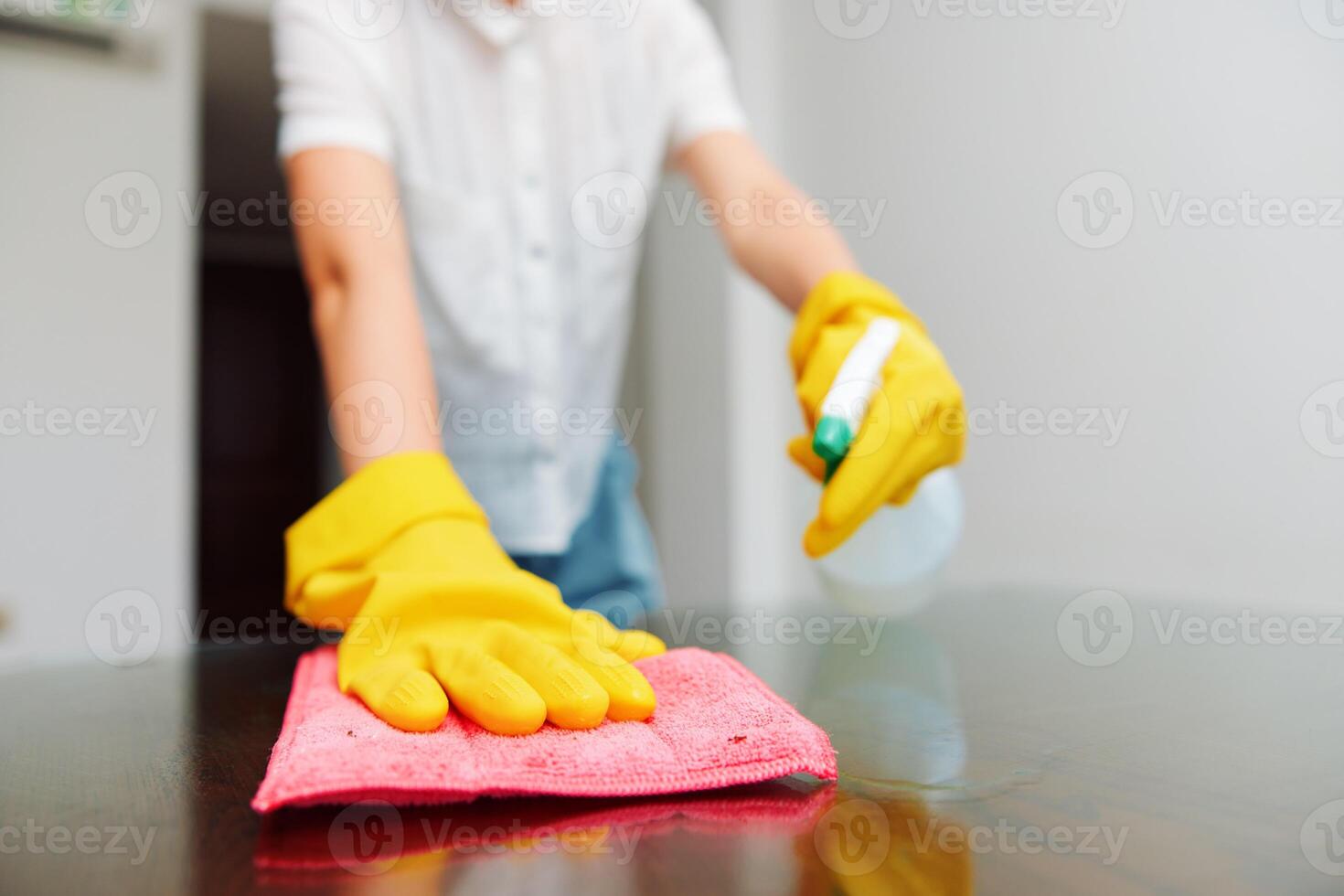 Woman in yellow rubber gloves cleaning table with cleaning solution bottle and rag on top. photo