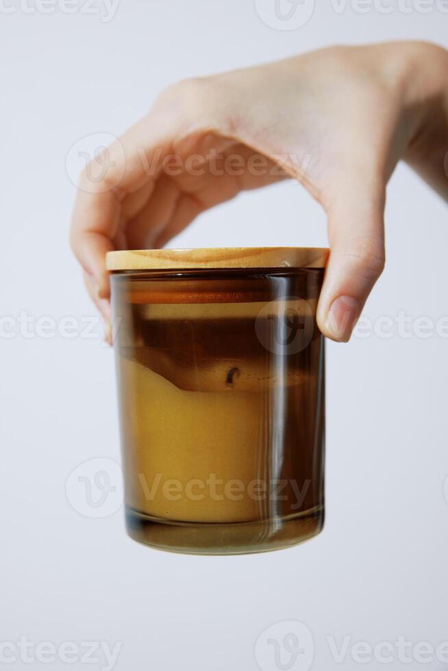 Person holding candle with wooden lid on glass jar in front of white background. a cozy and warm photo