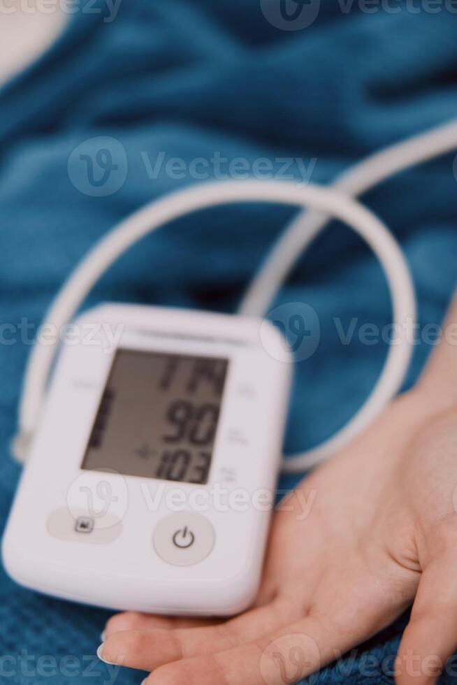 Person, holding, blood pressure monitor, hand, laying, bed, arm in air, digital monitor, next to photo