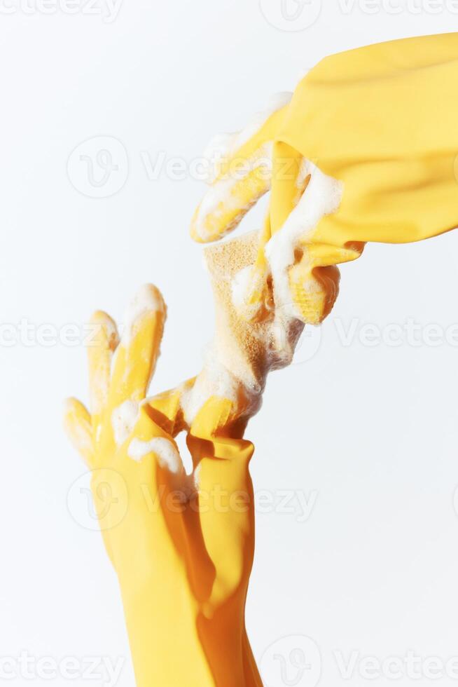 Rubber gloves and sponge on white background held up by hands. yellow household cleaning supplies photo