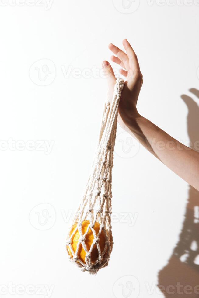 White macrame handbag with orange details held by a hand against a white background. mockup for photo