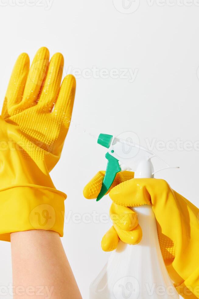 Woman in yellow rubber gloves holding a spray bottle and disinfectant on a white background photo